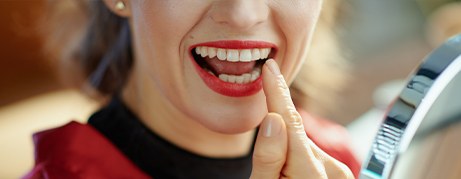 Woman with red lipstick looking at her teeth in a mirror