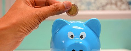 Hand inserting coin into blue piggy bank