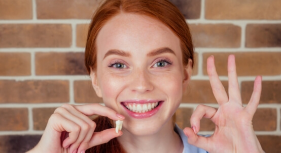 Smiling woman holding a tooth after a tooth extraction in Commack