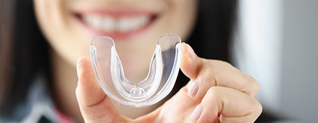 Smiling woman holds transparent plastic mouth guard in her hand