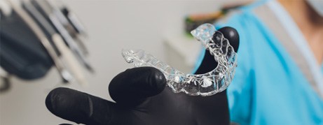 Dentist with black glove holding clear aligner