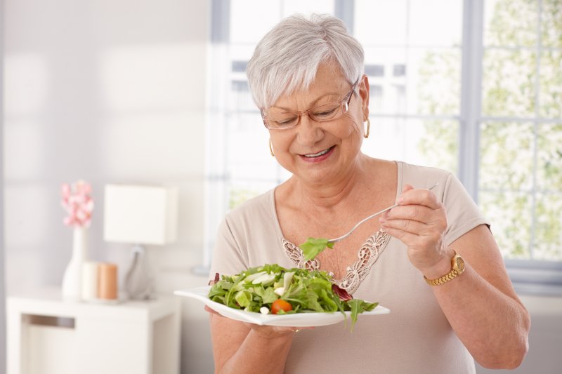 An older woman smiling and eating a green salad