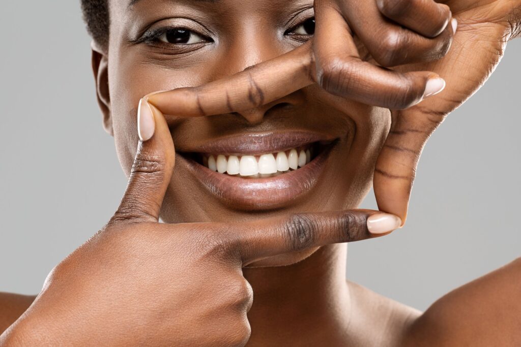 Facial closeup of woman framing her smile with thumbs and pointers